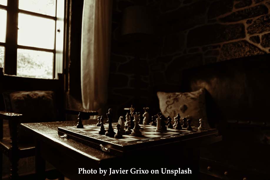 A chess board on a table near a window in a dim rustic room with stone walls.